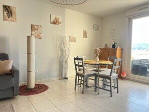 A modern living room with a sofa, a dining table with chairs, a tall floor lamp, and a view through a large window. - Le Cocon Provençal, 2-room apartment in downtown Hyères (Hyères)