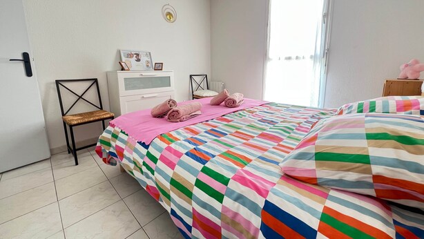 A bedroom with a bed, a chair, a bedside table, a window, and wall decorations. - Le Cocon Provençal, T2 Downtown Hyères (Hyères)