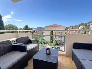 Ein Balkon mit Korbmöbeln und einem Tisch, mit Blick auf eine Wohngegend mit Häusern und Grünflächen.
