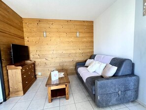 Un salon chaleureux avec un mur en bois, un canapé gris, une table basse en bois et un téléviseur posé sur un meuble en bois.