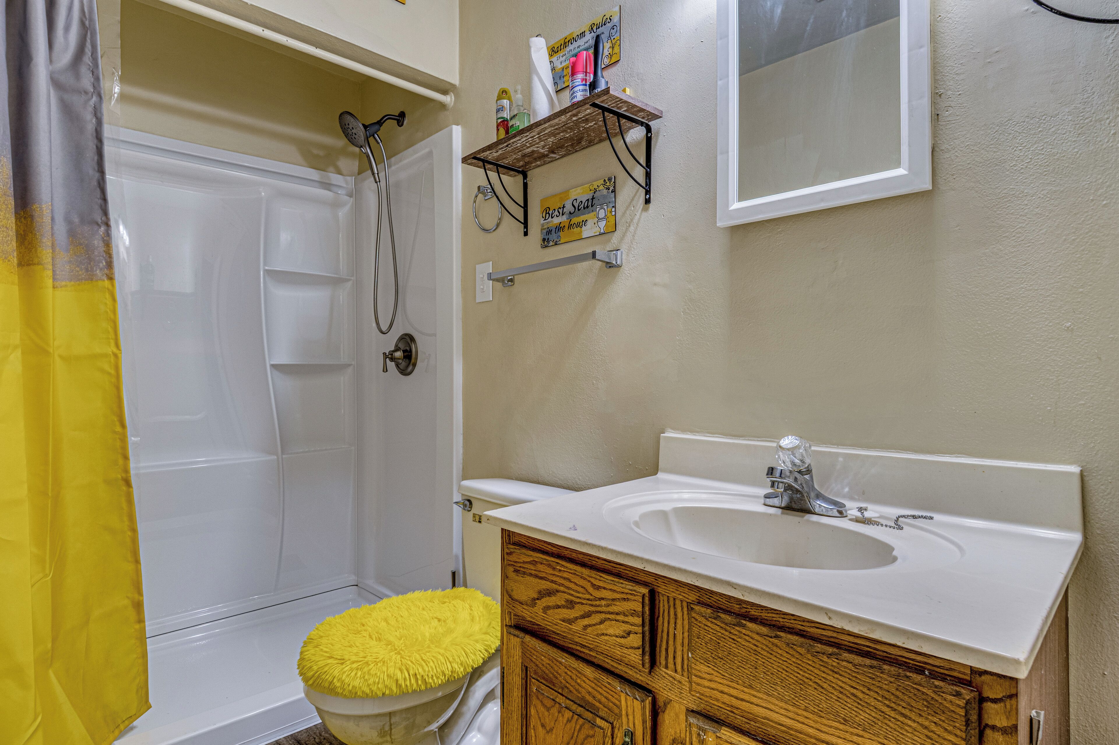 Un baño con ducha, lavabo, armarios de madera y una pequeña estantería con artículos de aseo.