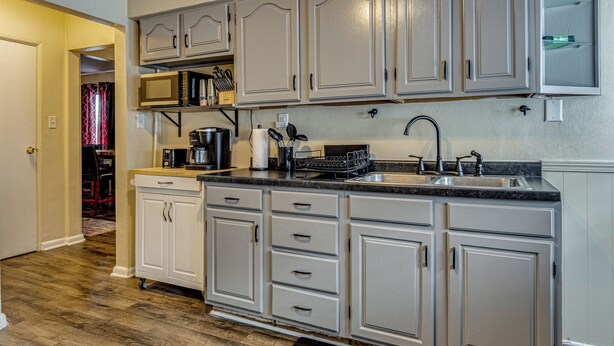 A kitchen with white cabinets, a microwave, a coffee maker, and a sink.