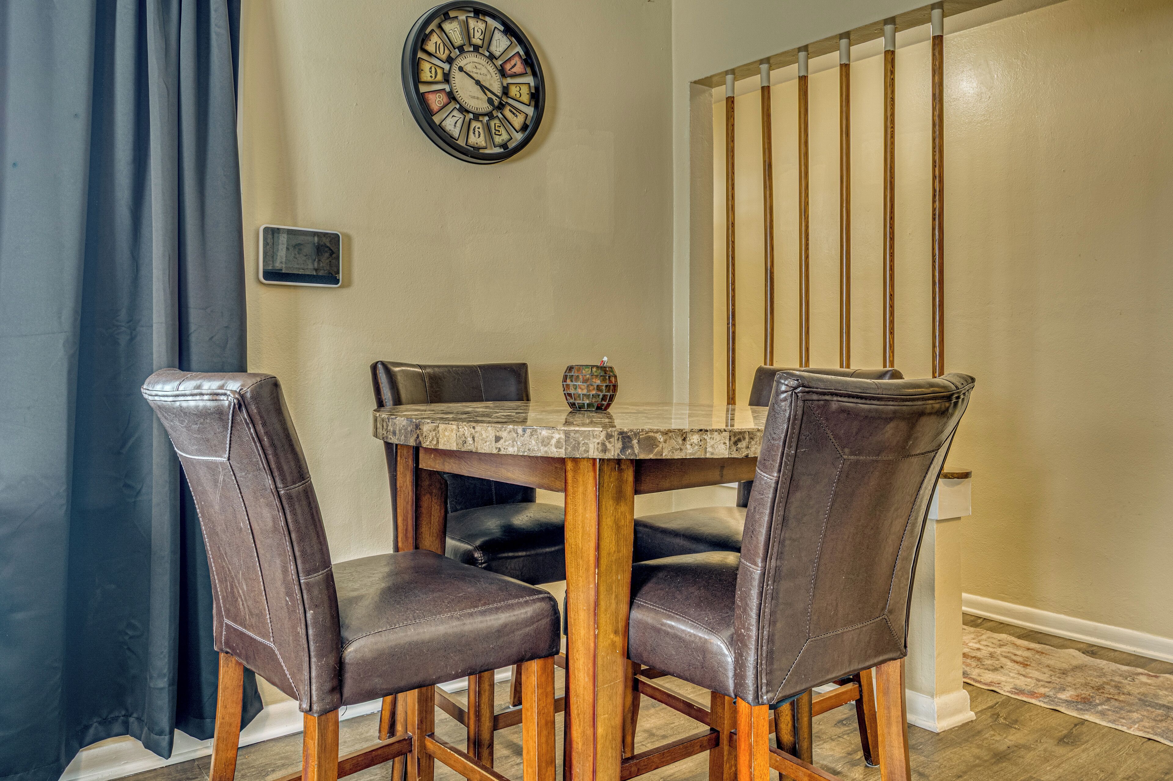 A dining area with a round table, four leather chairs, a clock on the wall, and a vertical wooden panel.