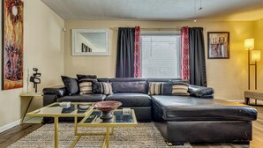 A modern living room with a sectional sofa, a glass coffee table, and a large painting on the wall.