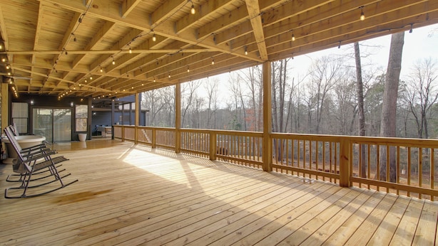 A wooden deck with a railing, rocking chairs, and a view of trees. - Mountain Retreat in Commerce w/ Billiards + Darts (Commerce)