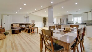A spacious living area with a wooden dining table, multiple chairs, a sofa, and a kitchen in the background. - Mountain Retreat in Commerce w/ Billiards + Darts (Commerce)