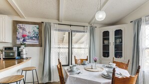 Un comedor con una mesa dispuesta para cuatro personas, sillas de madera, mantel blanco y un cuadro en la pared.