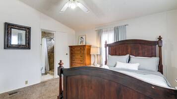 Un dormitorio con una cama de madera, un ventilador de techo, un aparador y un baño visible a través de una puerta abierta.