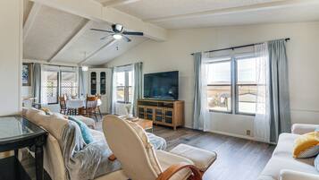 A spacious living room with a ceiling fan, a television on a wooden cabinet, and a dining area with a table and chairs.