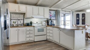 Una cocina con muebles blancos, horno empotrado y una isla grande con acabado similar a la piedra.