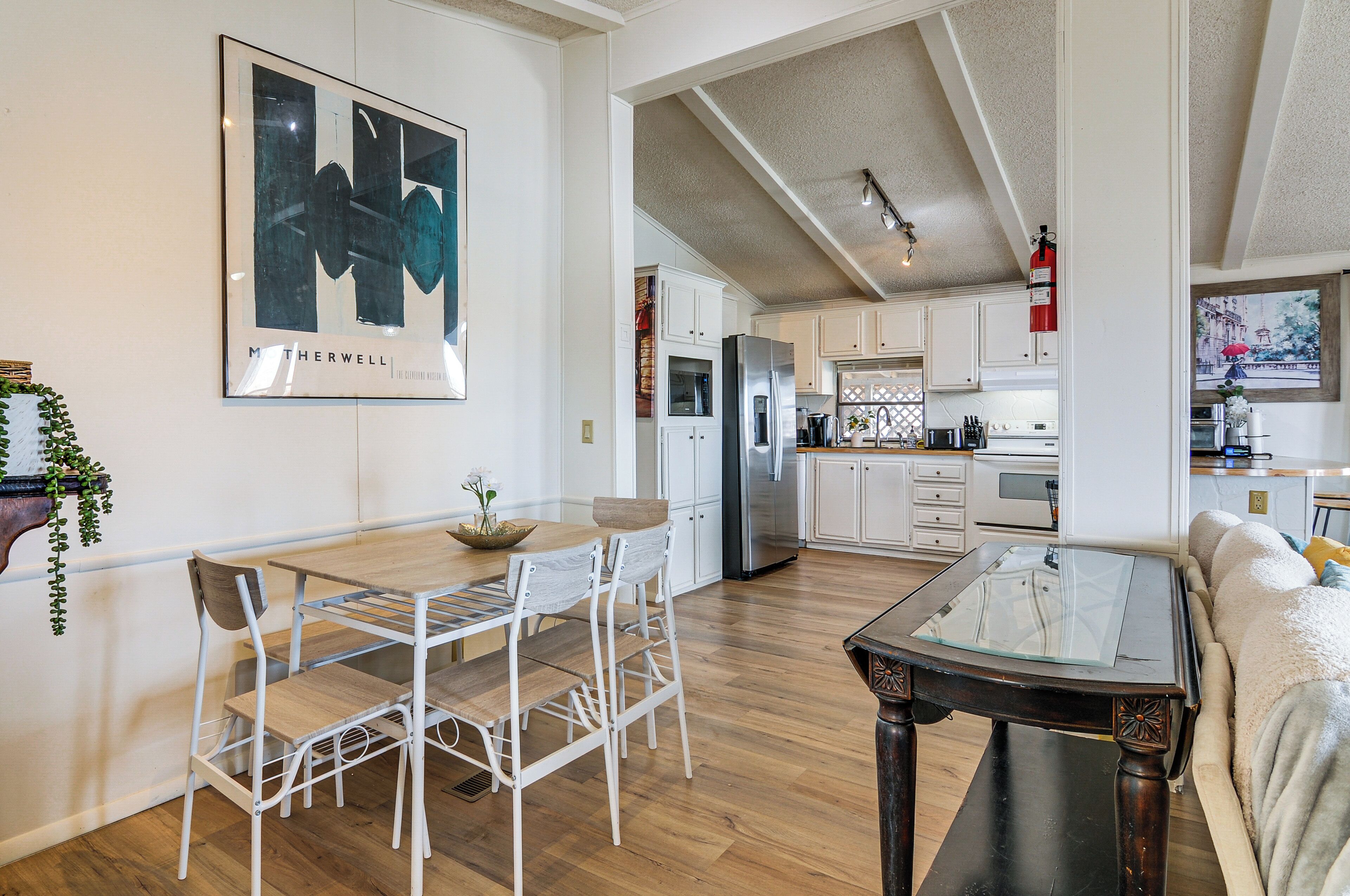 A modern kitchen with white cabinets, stainless steel appliances, and a dining area with a glass-top table and white chairs.