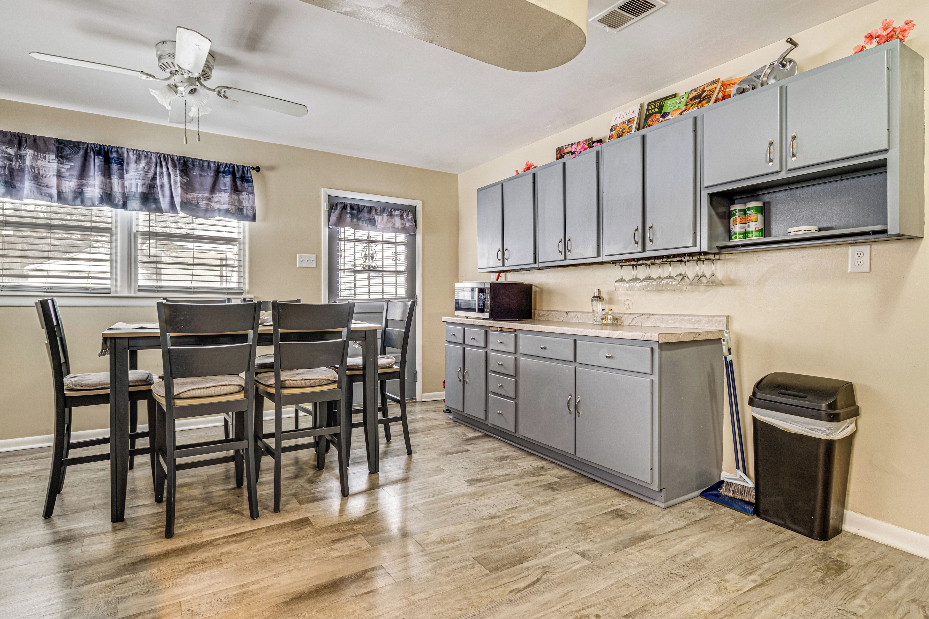 A kitchen with a dining table and chairs, gray cabinets, a ceiling fan, and a trash can.