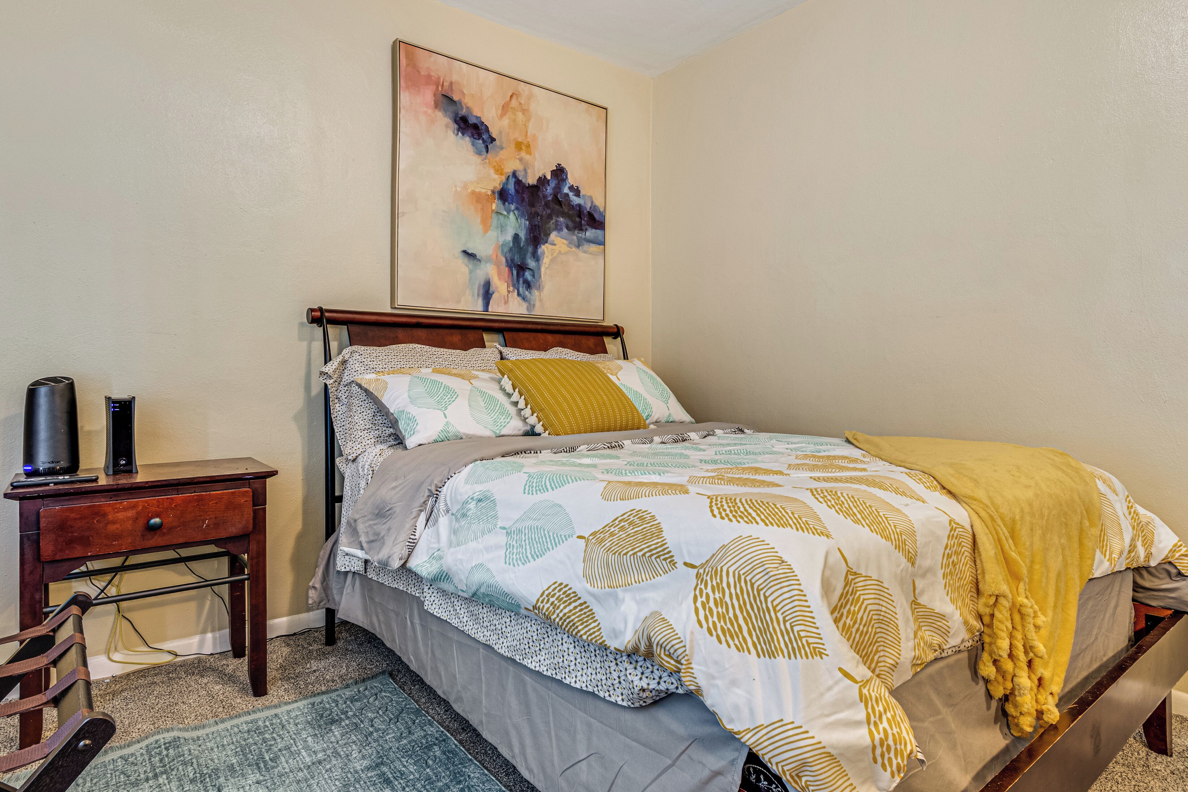 A bedroom with a bed, a nightstand, a lamp, and a painting on the wall.