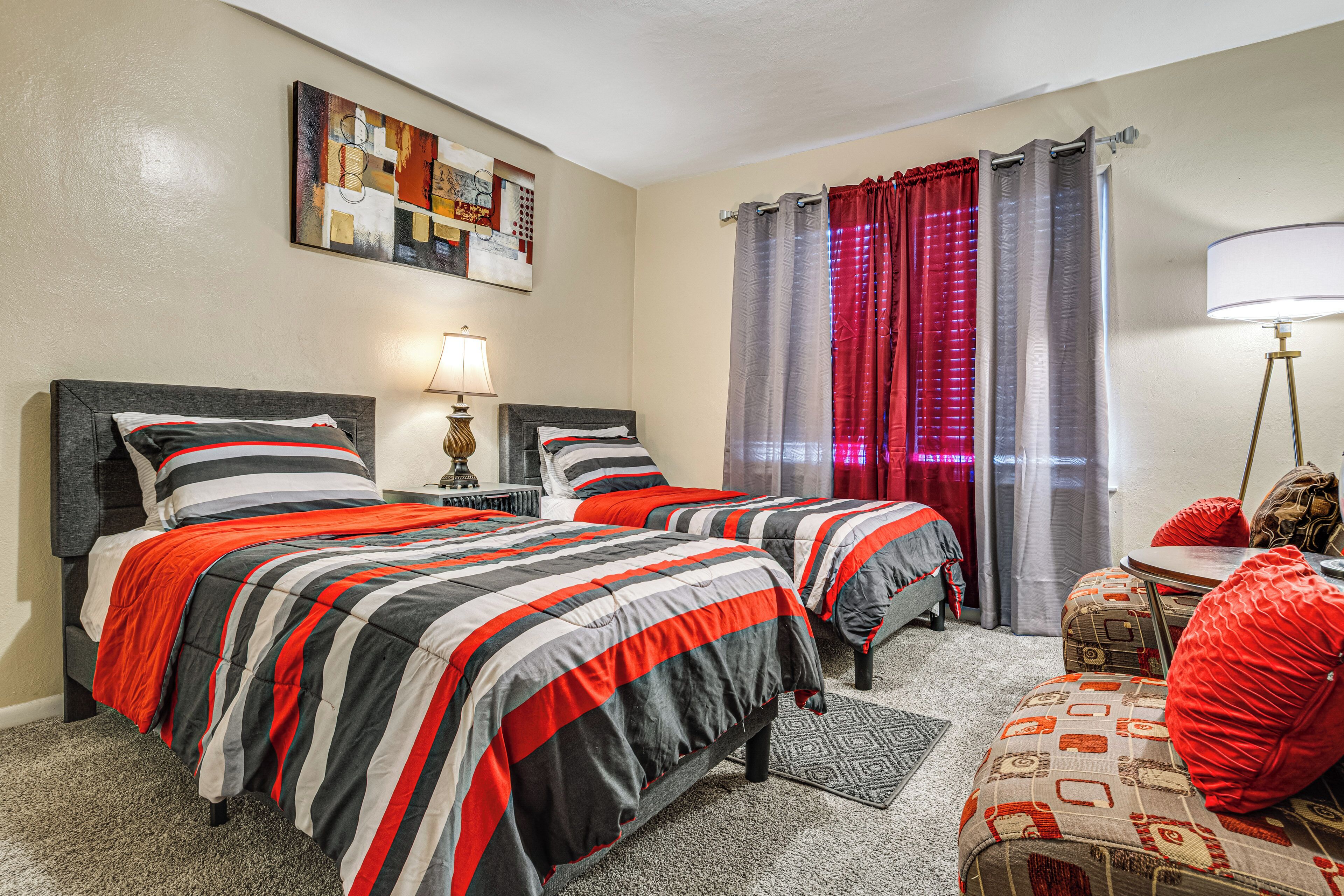 A hotel room with two beds, a small table, a lamp, and a painting on the wall.