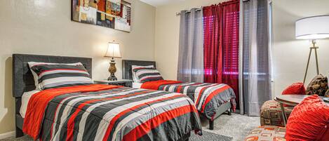A hotel room with two beds, a small table, a lamp, and a painting on the wall.