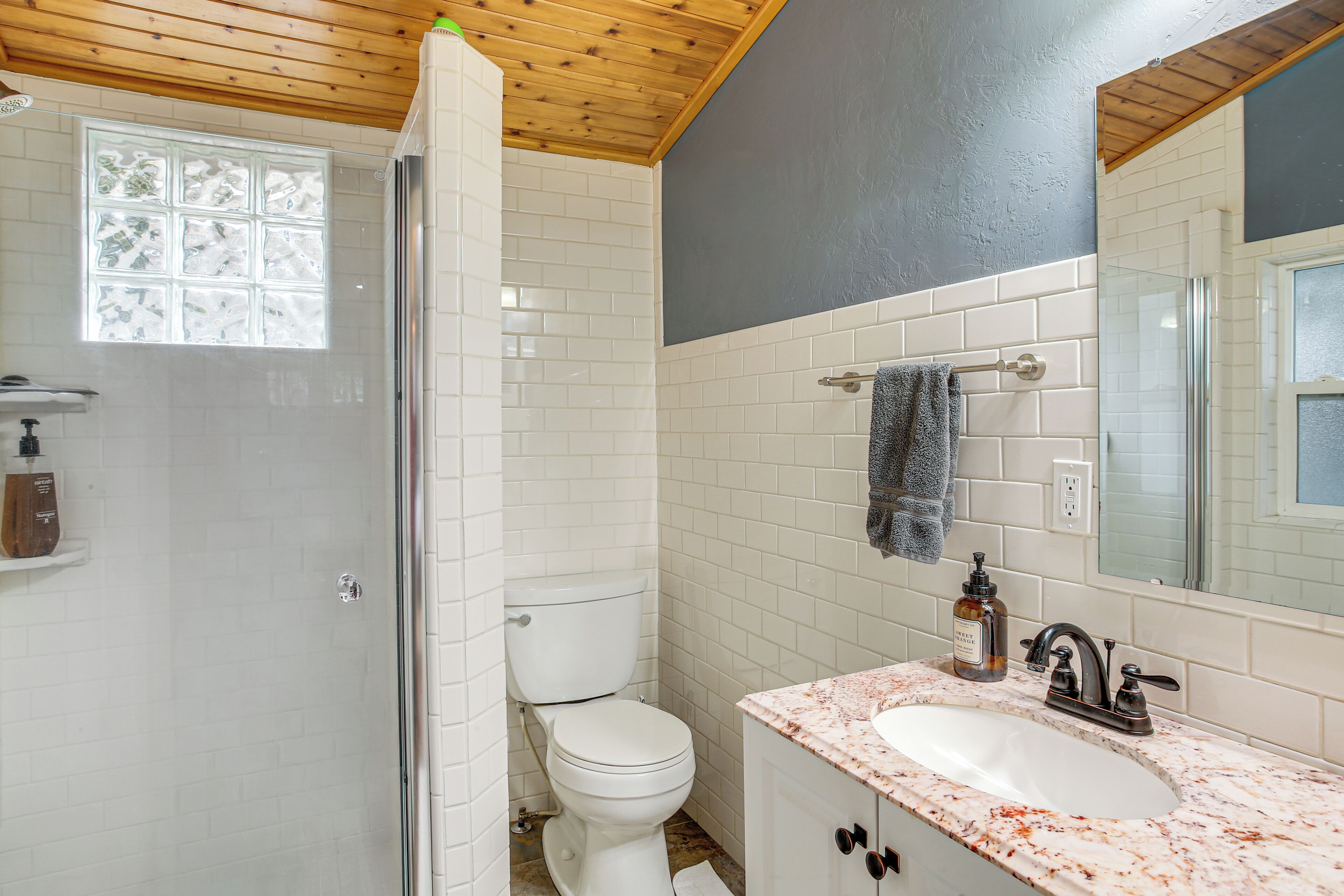Une salle de bain avec des toilettes blanches, une douche en verre, un lavabo en marbre et un miroir au-dessus du lavabo.