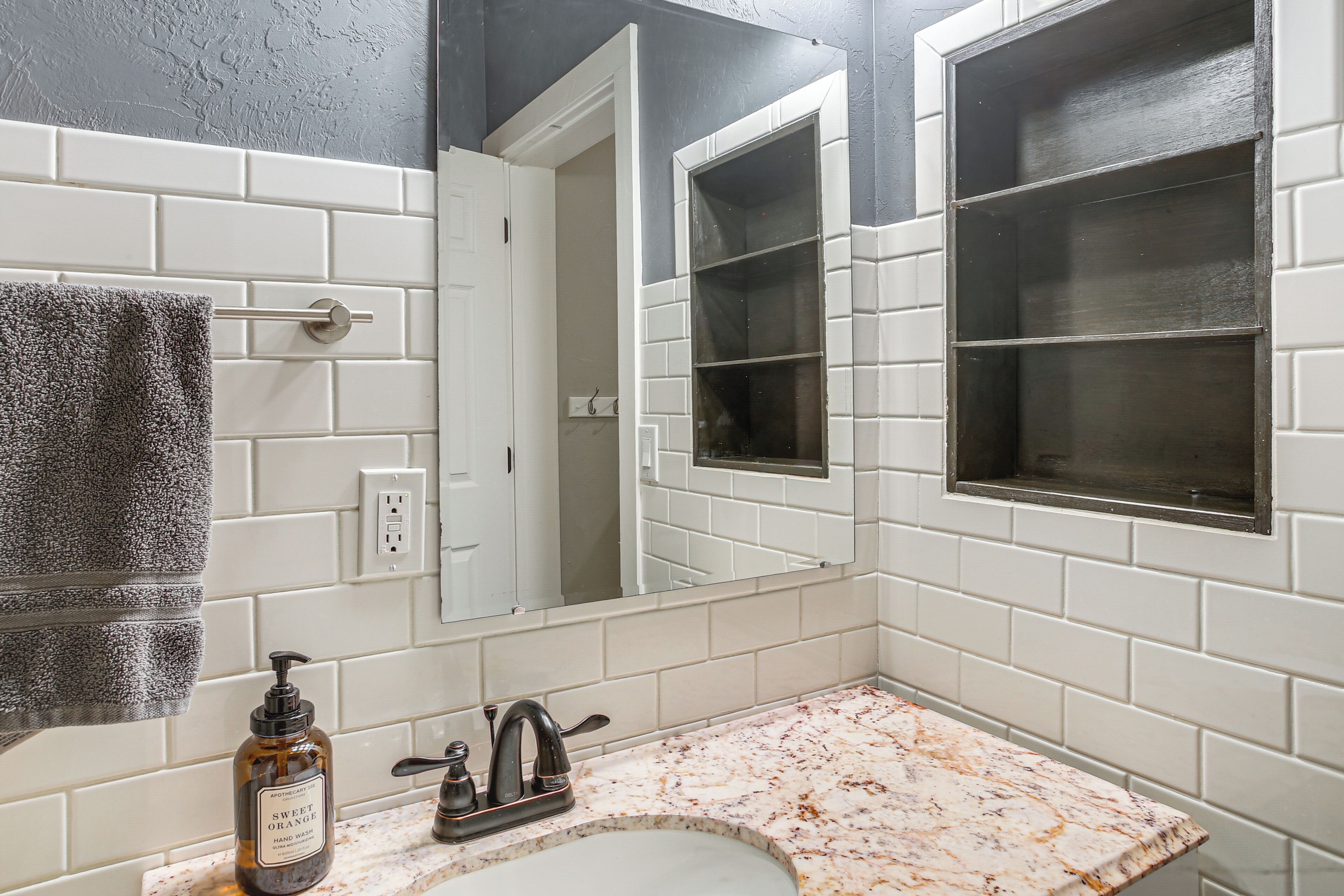 A bathroom with white subway tiles, a marble countertop, a sink, a mirror, and a towel hanging on the wall.