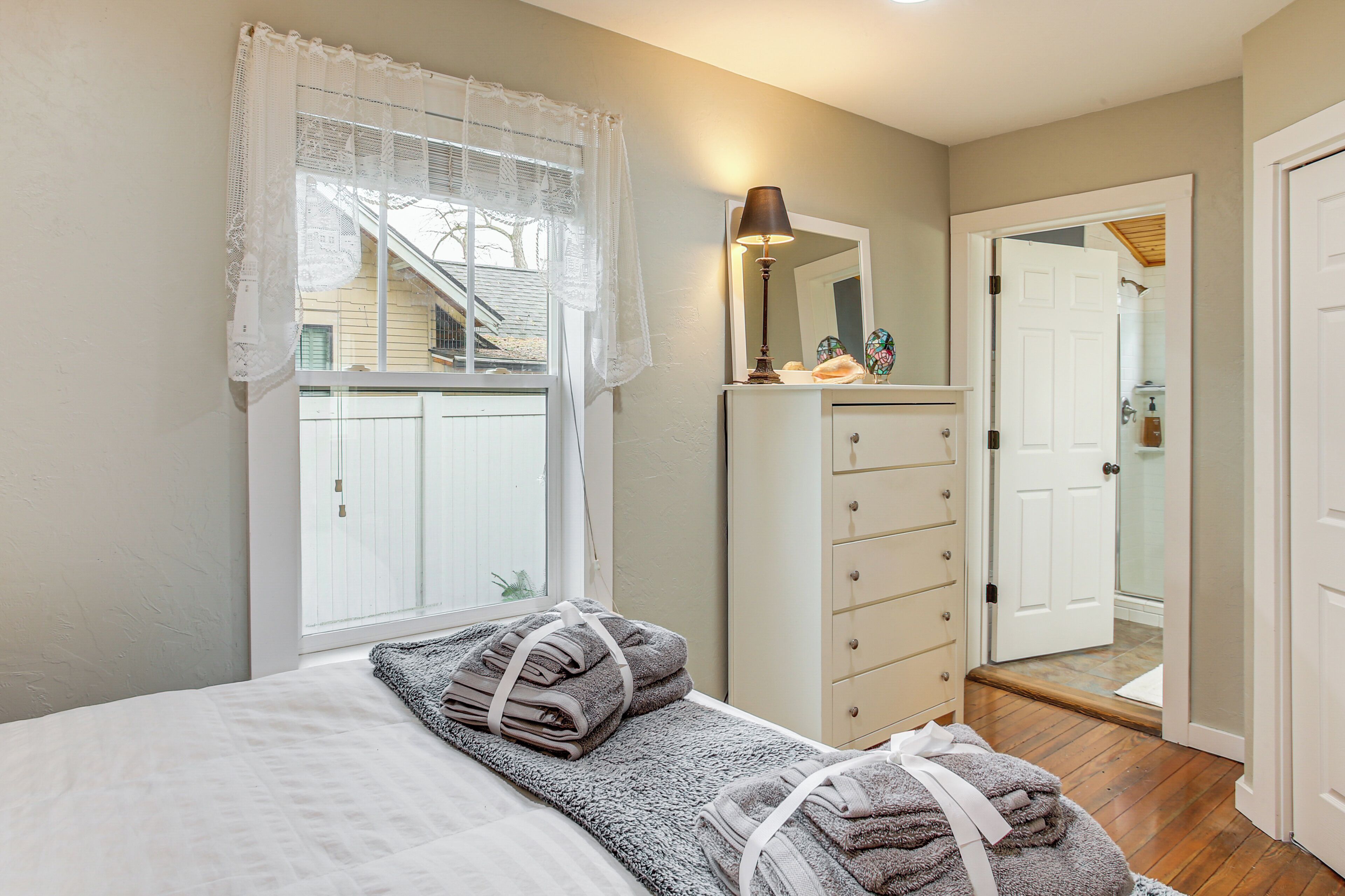 Un dormitorio con cama, cómoda, espejo y ventana con cortinas.