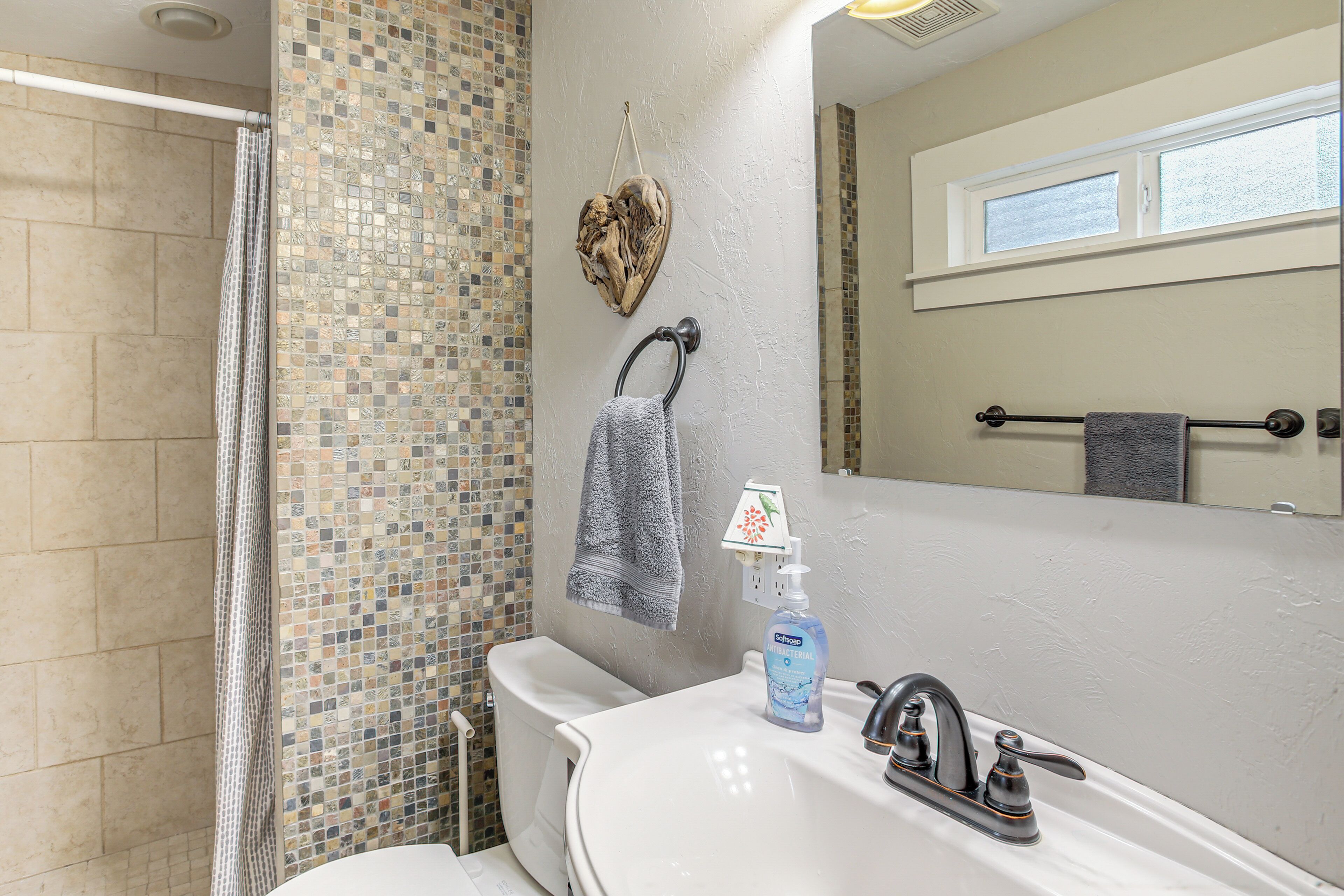 A bathroom with a shower, a toilet, a sink with a soap dispenser, and a towel rack.
