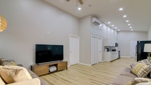A spacious living room with a flat-screen TV, wooden flooring, and a kitchenette in the background. - Gateway to North Georgia Mtns! Commerce Retreat (Commerce)