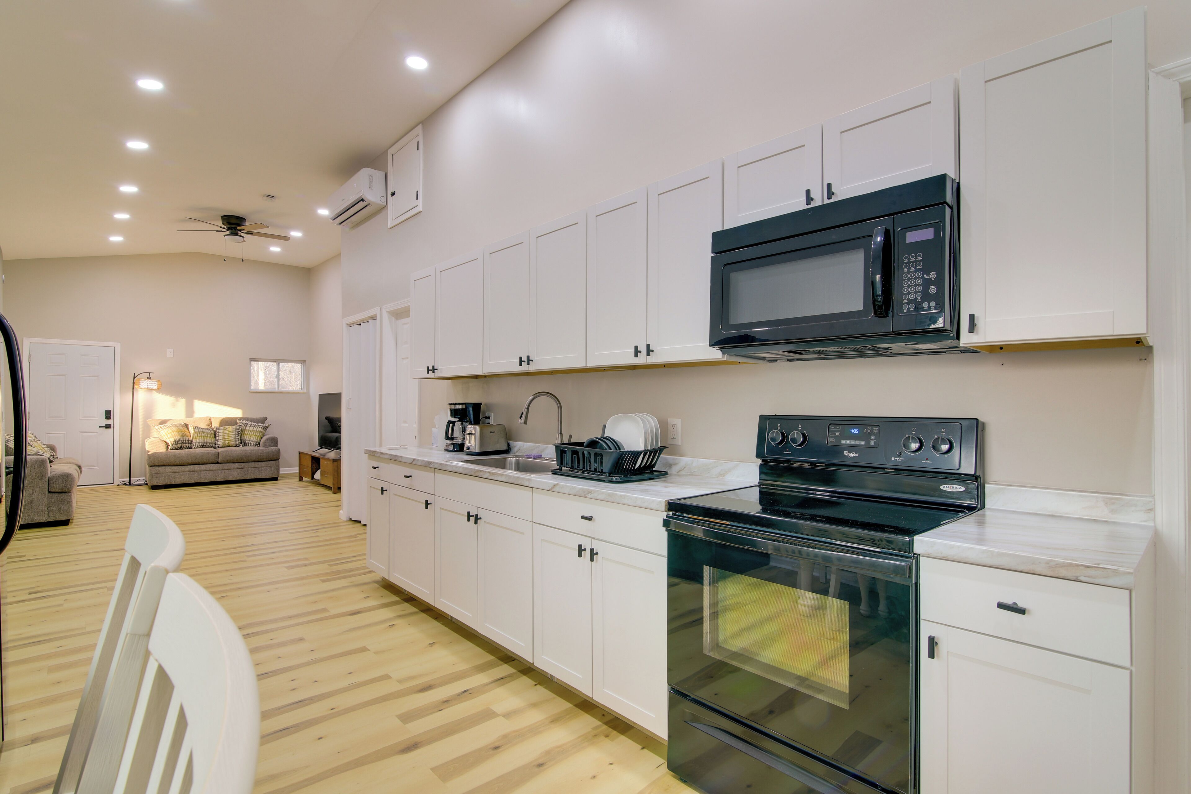 A modern kitchen with white cabinets, a black microwave, a stove, and a sink.
