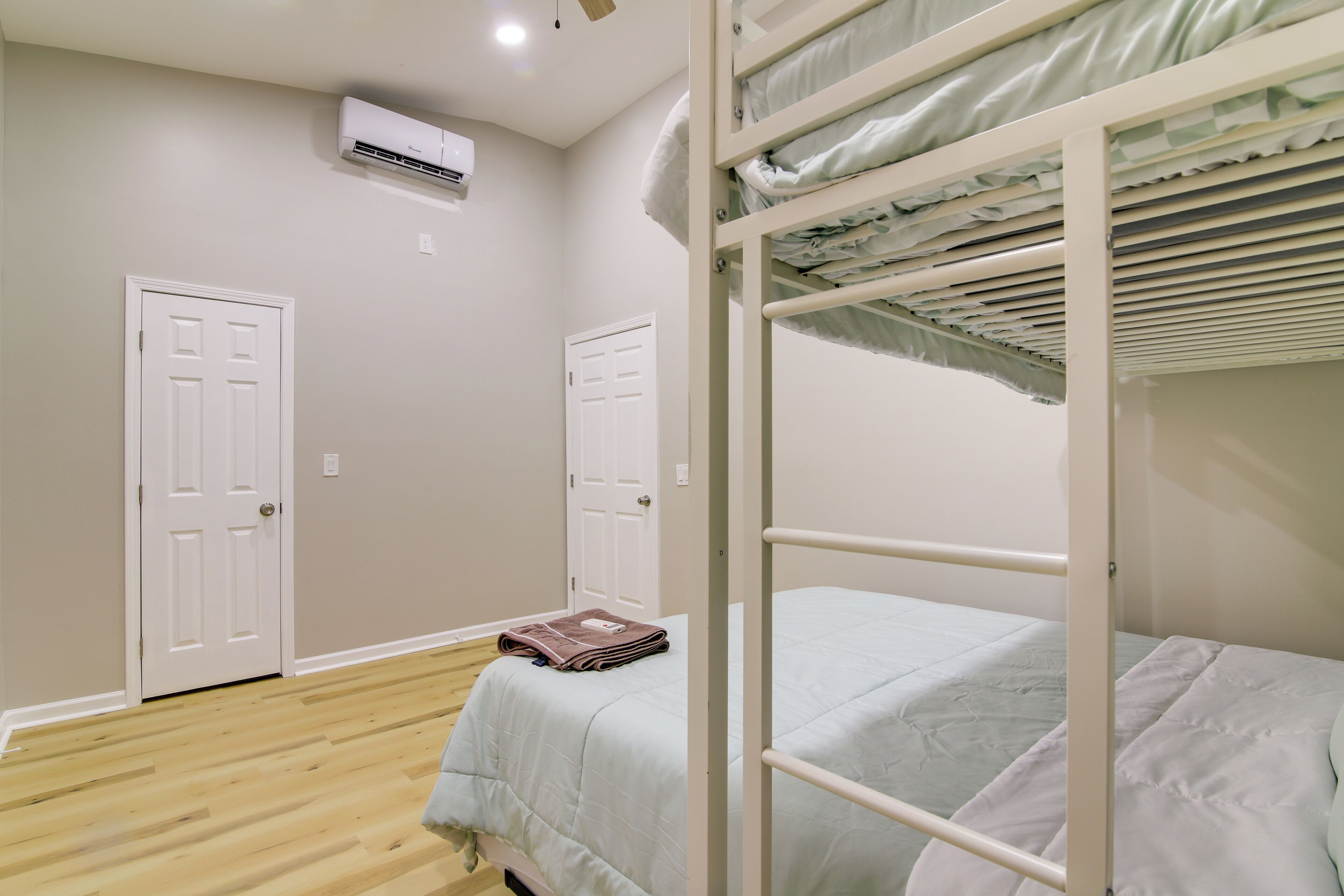 A bedroom with a bunk bed, two white doors, an air conditioning unit, and a wooden floor.