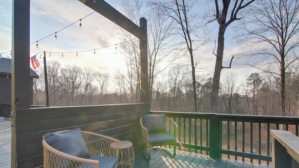 A wooden deck with wicker chairs and a table, overlooking a forested area. - Gateway to North Georgia Mtns! Commerce Retreat (Commerce)