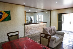 Ein Hotelzimmer mit Essbereich, einer Couch, einem Tisch mit rotem Tischläufer, einer Küchenzeile inklusive Kühlschrank und einer Glastür, die nach draußen führt.