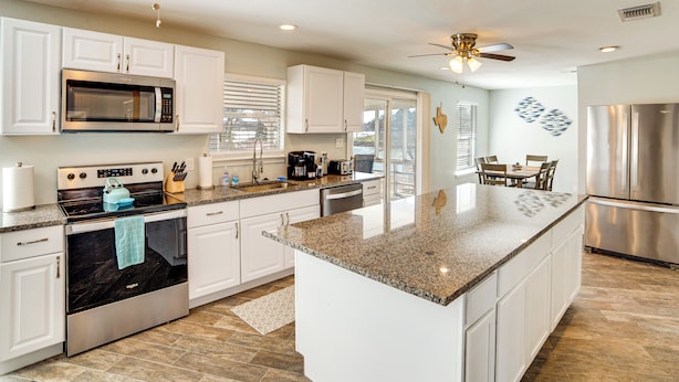A modern kitchen with white cabinetry, a large island, stainless steel appliances, and a dining area with a table and chairs. - Lakeside Retreat: Large Spacious Home w/ Game Room (Kemp)