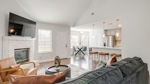 A modern living room with a fireplace, a large grey sofa, and a dining area with a table and chairs. - Walk to the Greenline: Sleek Cordova Home w/ Patio (Cordova)