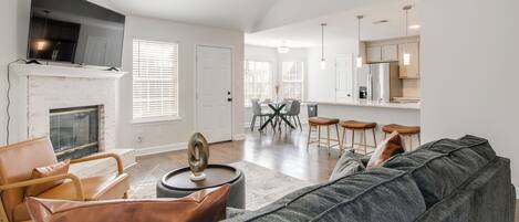 A modern living room with a fireplace, a large grey sofa, and a dining area with a table and chairs.