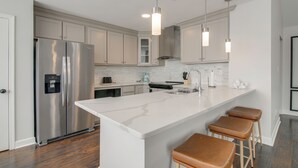 A modern kitchen with a stainless steel refrigerator, white marble countertop, and pendant lighting. - Walk to the Greenline: Sleek Cordova Home w/ Patio (Cordova)