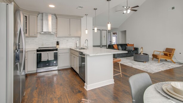 A modern kitchen with white cabinetry, a central island, and a dining area with a gray table and chairs. - Walk to the Greenline: Sleek Cordova Home w/ Patio (Cordova)