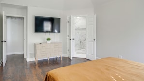 A bedroom with a bed, a TV mounted on the wall, a dresser, and a door leading to another room. - Walk to the Greenline: Sleek Cordova Home w/ Patio (Cordova)