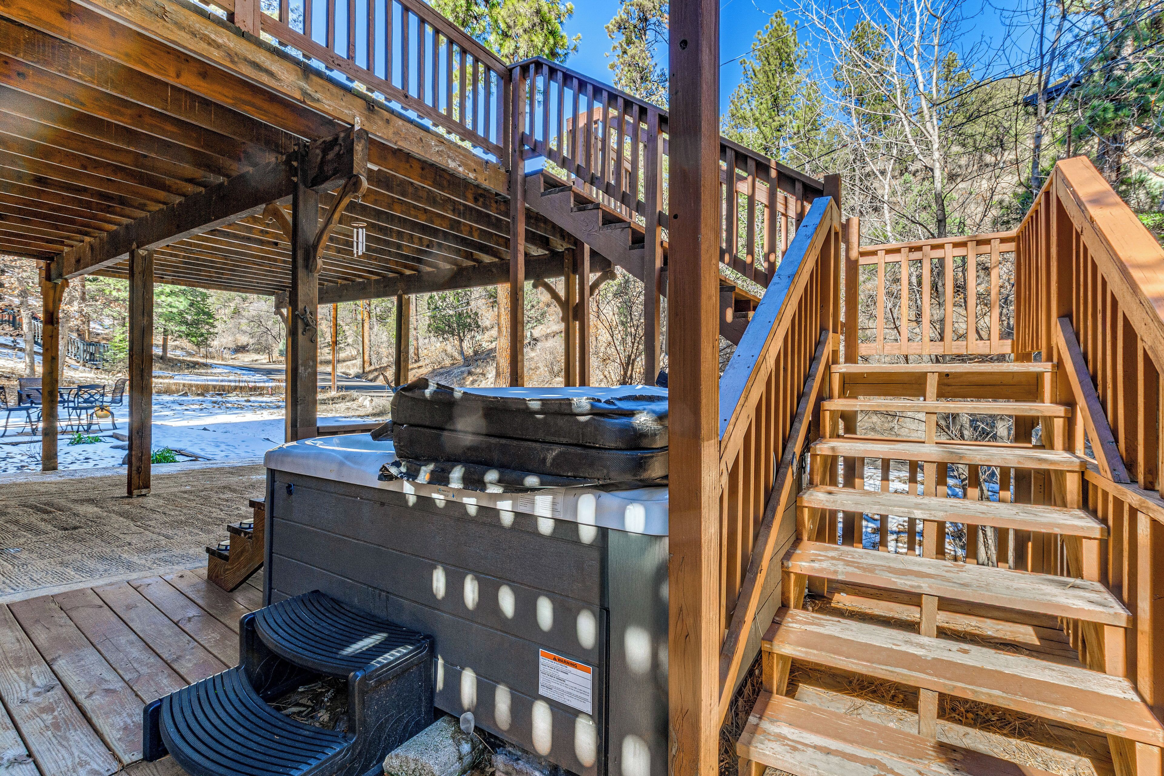 A wooden deck with a hot tub, outdoor seating, and a staircase leading to an upper level.