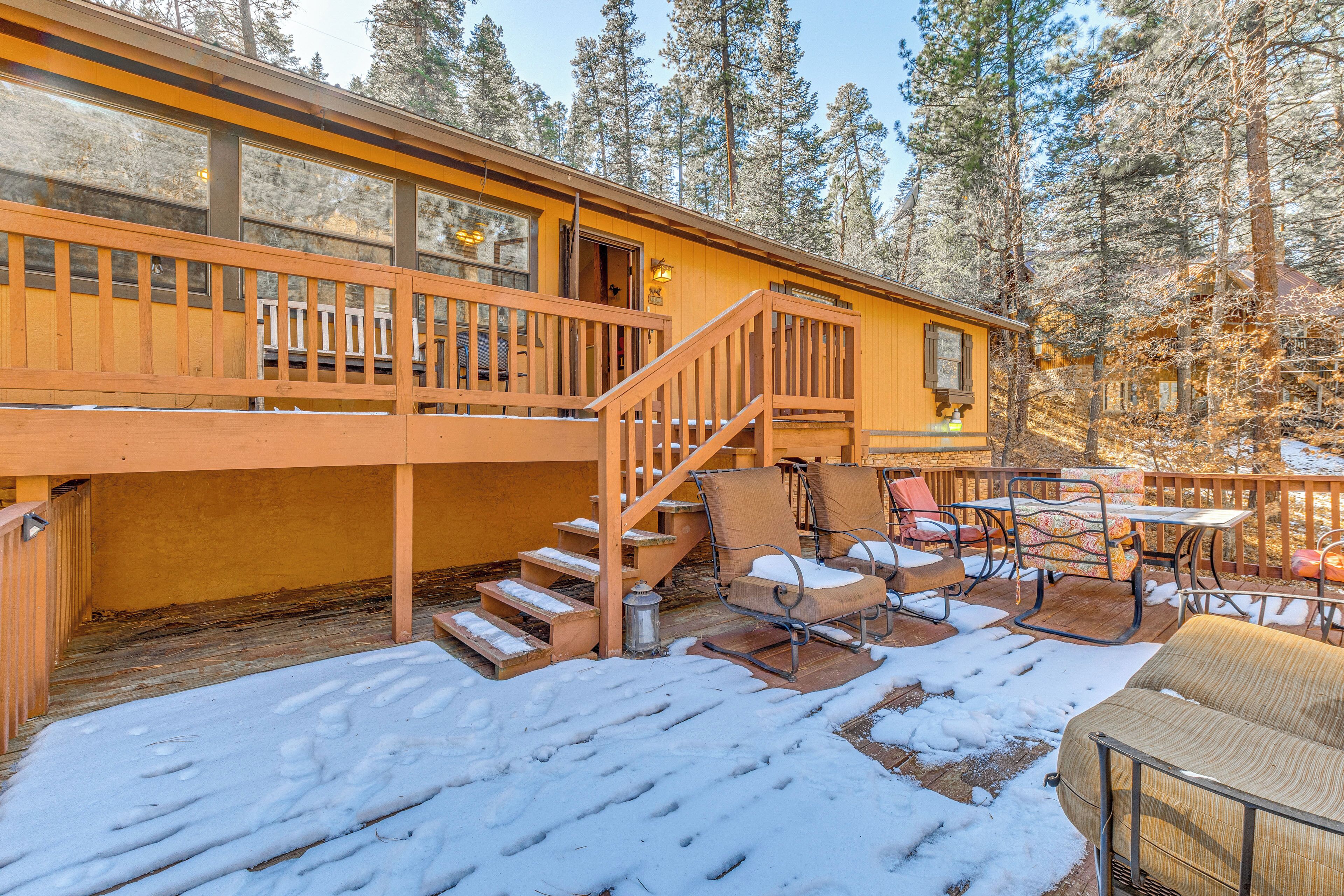 A wooden cabin with a deck, outdoor seating, and a staircase leading to an upper level.