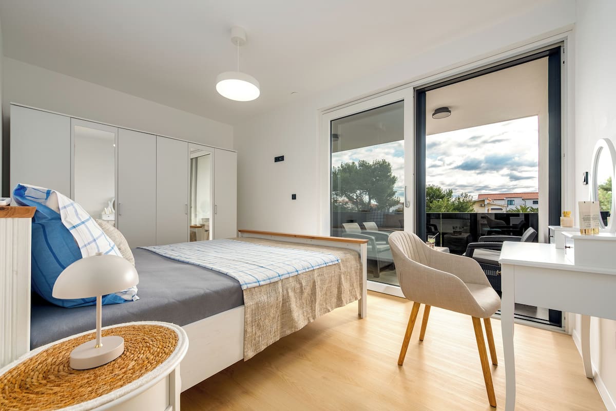 A modern bedroom with a bed, bedside table, lamp, and a view through a large window.