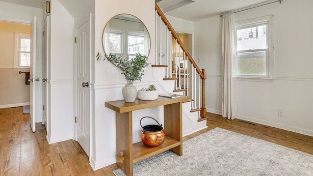 A hallway with a wooden console table, a mirror, a vase, and a copper pot.