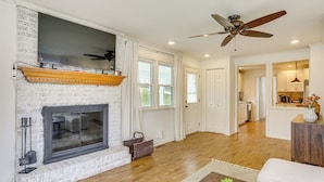 A spacious living room with a fireplace, wooden flooring, and a ceiling fan.