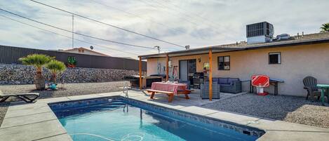 Un patio trasero con piscina, zona de barbacoa y aro de baloncesto.