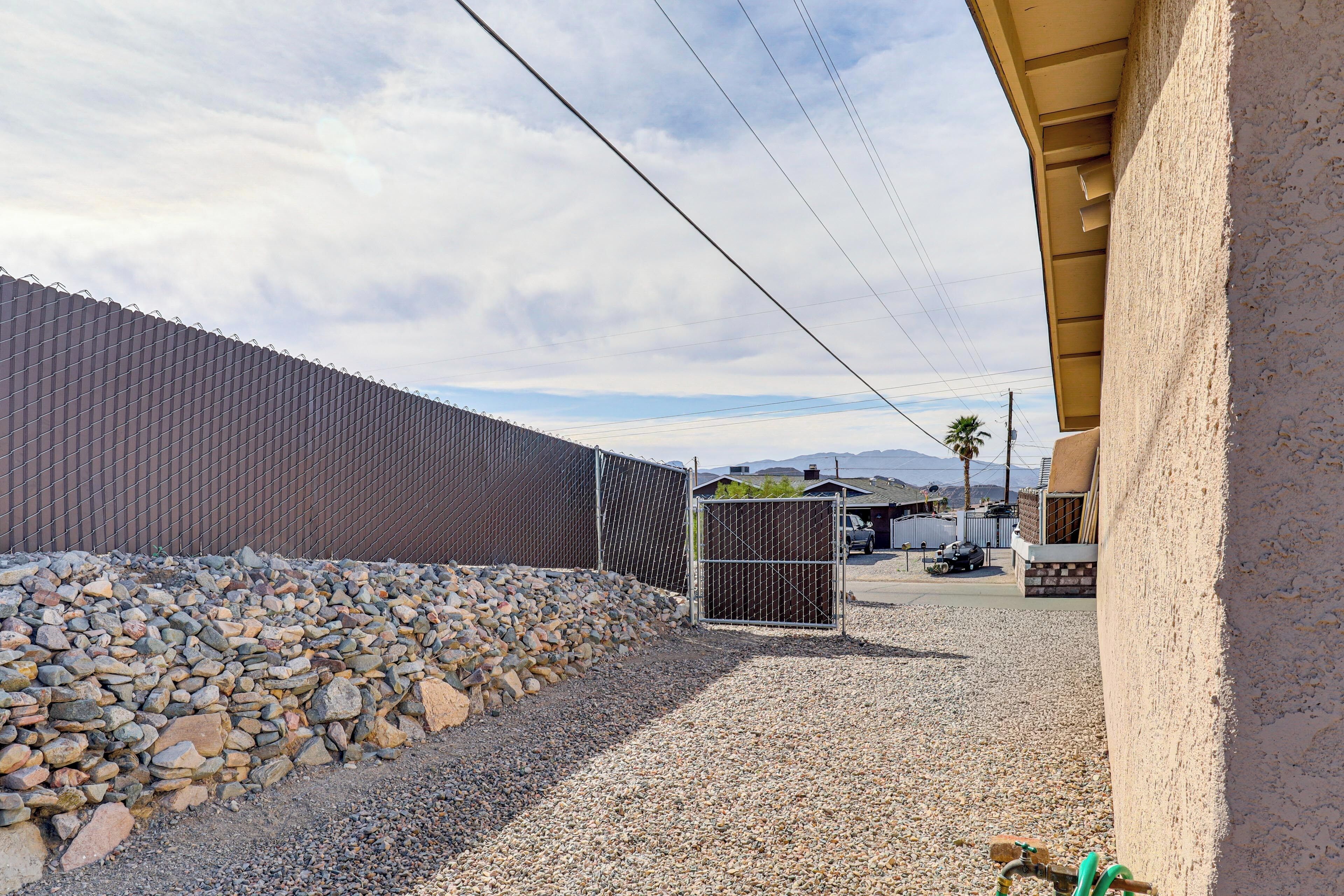 A gravel driveway leading to a gated area with a chain-link fence, a small utility shed, and a building with a stucco exterior.