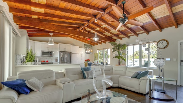 A spacious living area with a white leather sofa, a glass coffee table, and a wooden ceiling with exposed beams. - Oakland Park Gem w/ Year-round Pool, 4 Mi to Beach (Fort Lauderdale)