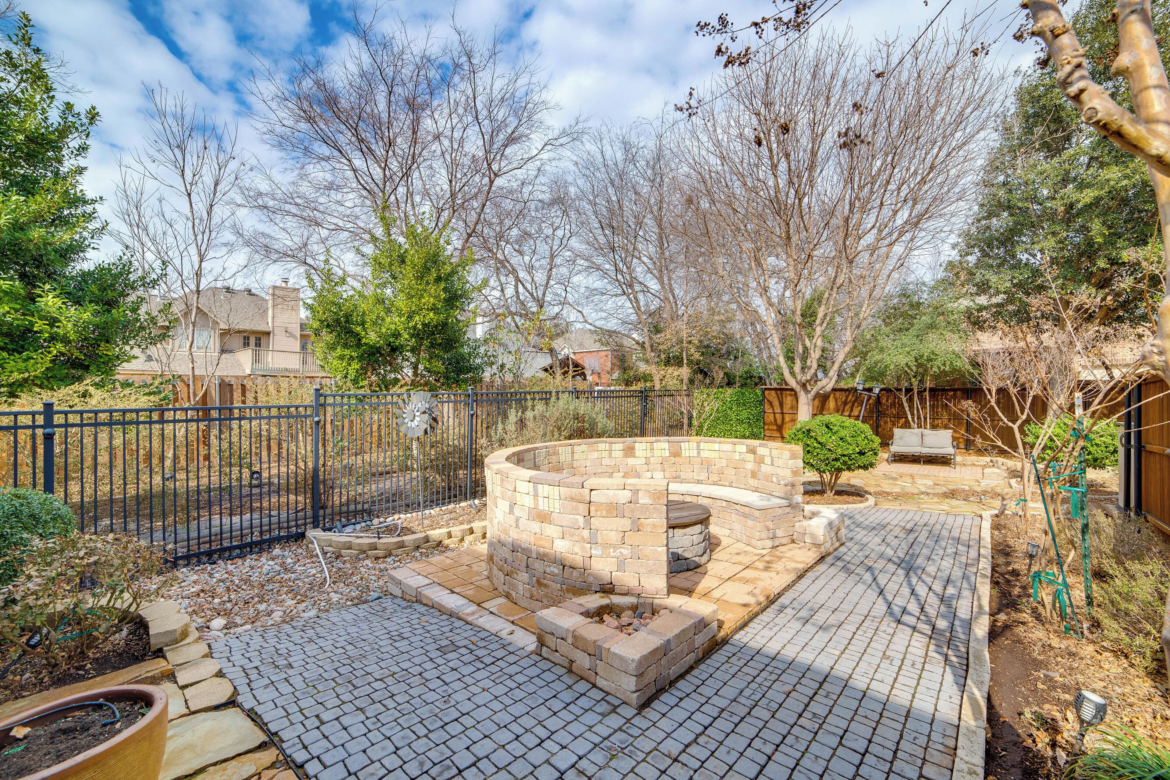 A backyard with a brick fire pit, a paved patio, and a fenced area.