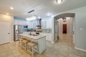 Una cocina moderna con armarios blancos, una isla grande con taburetes de bar, electrodomésticos de acero inoxidable y una lámpara de araña.
