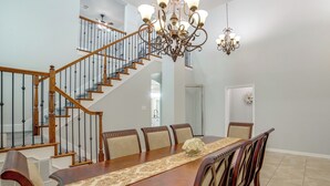 Ein Esszimmer mit Holztisch, Stühlen, einer Chandelierleuchtre und einer Treppe.