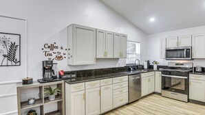 Eine moderne Küche mit weißen Schränken, einem Edelstahlbackofen und einer Kaffeestation.