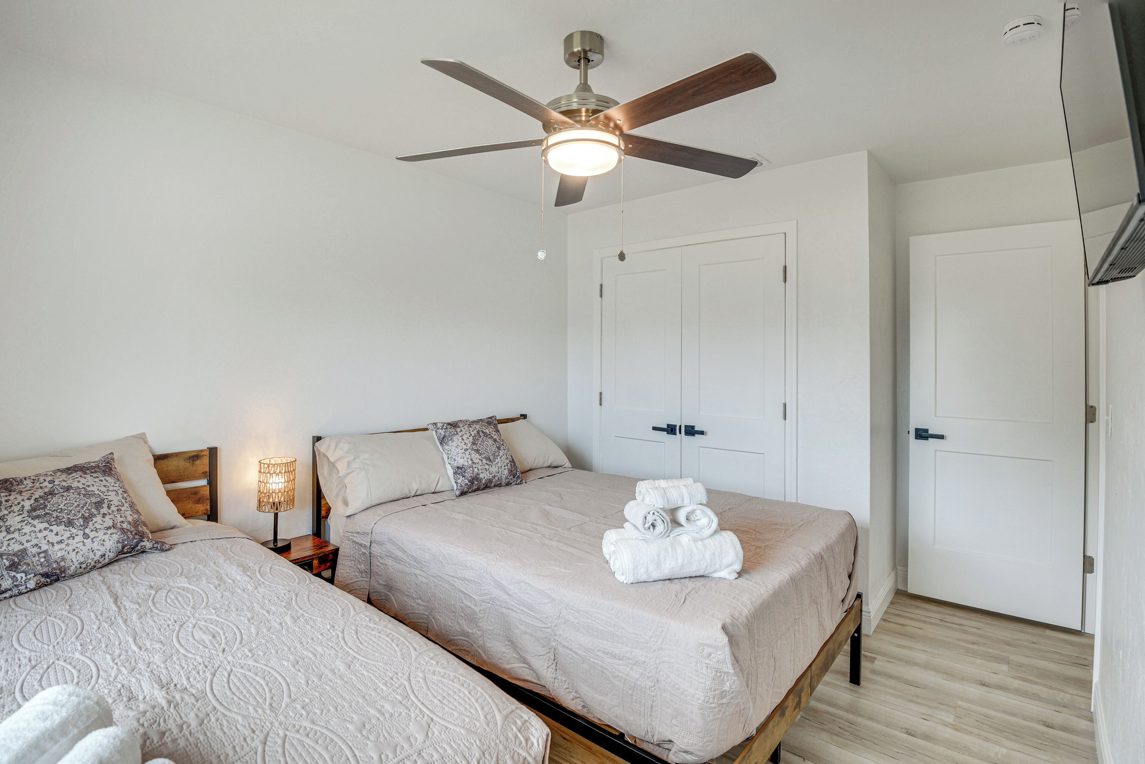 Une chambre avec deux lits, un ventilateur de plafond, une lampe de chevet et une armoire.