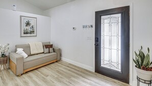 Ein Wohnzimmer mit einer Couch, einer Tür mit Glasfenster, einer Wand-Klimaanlage und einer kleinen Pflanze.
