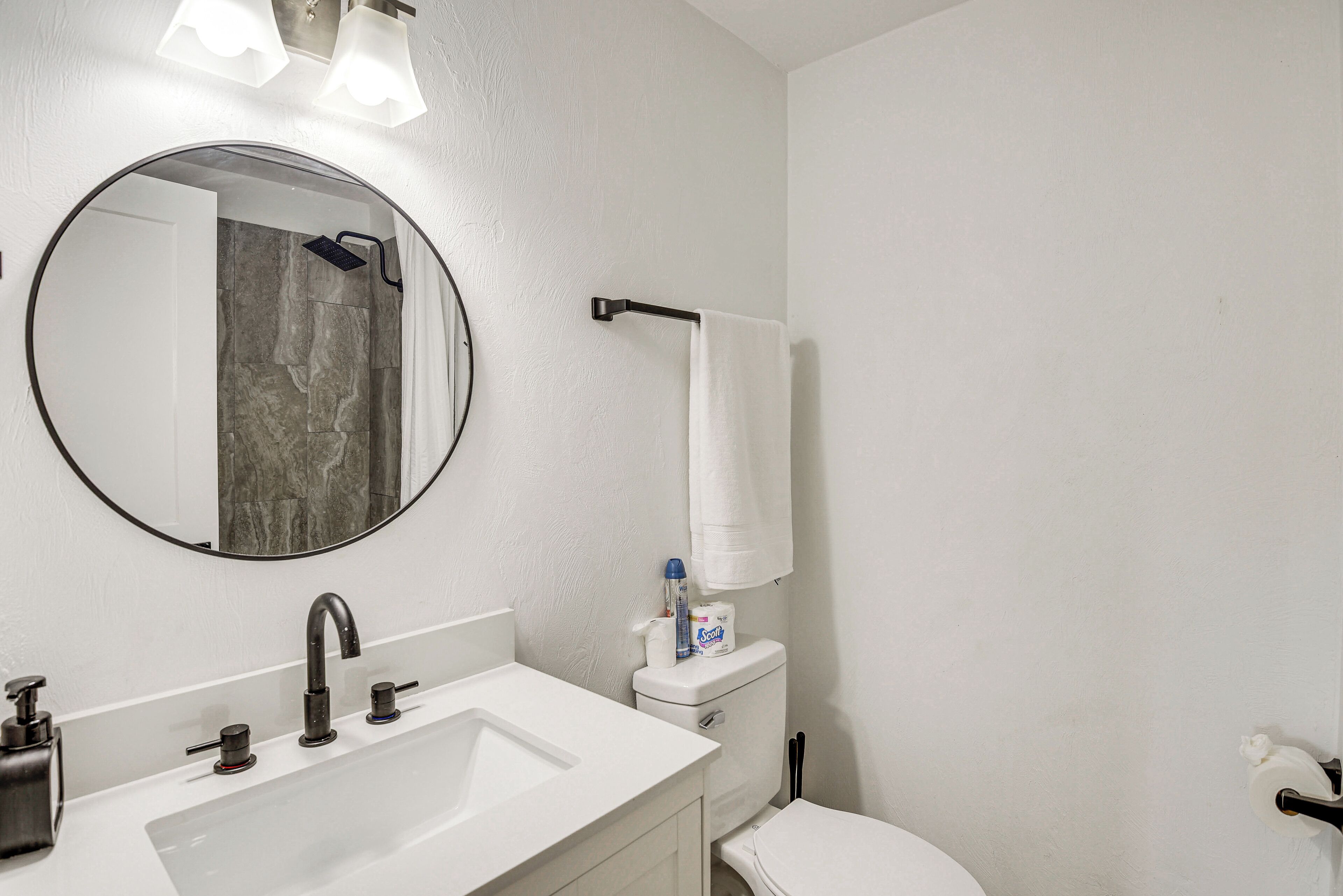 A bathroom with a round mirror, a white sink, a toilet, and a towel rack.