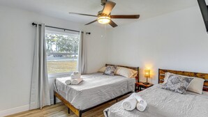 Ein Schlafzimmer mit zwei Betten, einem Deckenventilator, einem Fenster mit Vorhängen und einem Nachttisch mit Lampe.